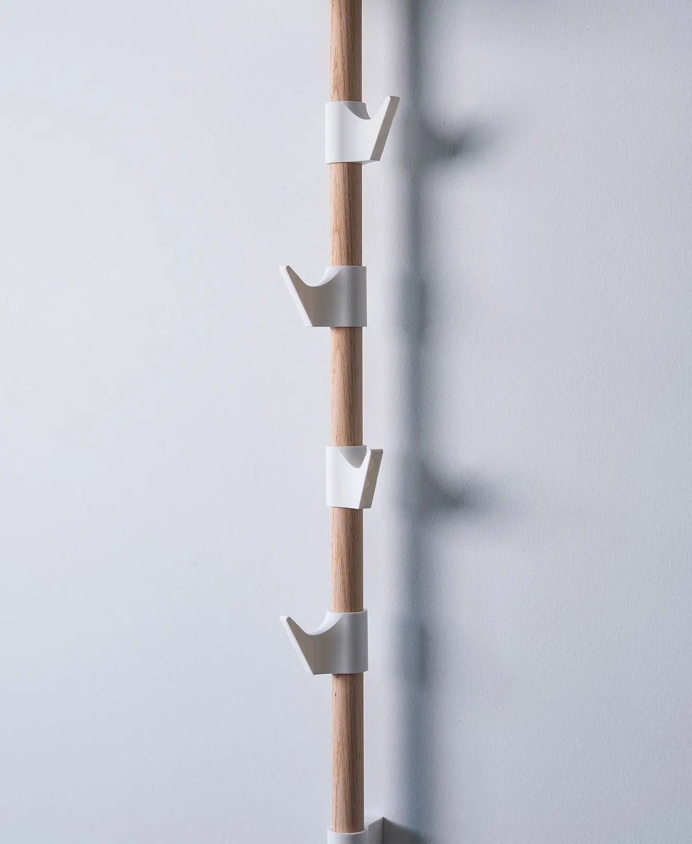 Mehrere weisse Haken am Evoliv Horizontal Rail System an einer vertikalen Holzschiene zur modularen Aufbewahrung.